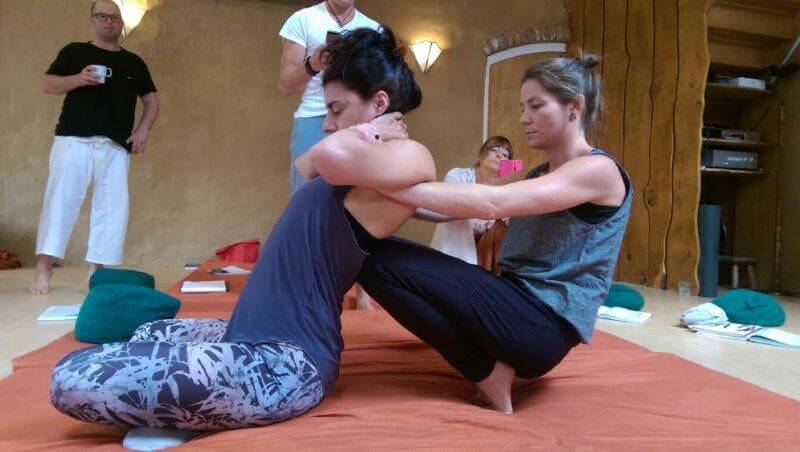 A lady stretching another lady's back using her knees while three people watching taking pictures of it