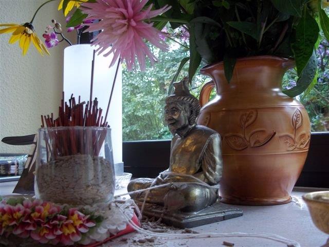 Close up shot of a plant vase, incense, and a small statue near window